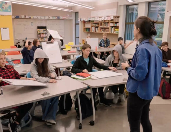 Teacher standing in front of engaged students sitting behind a desk 